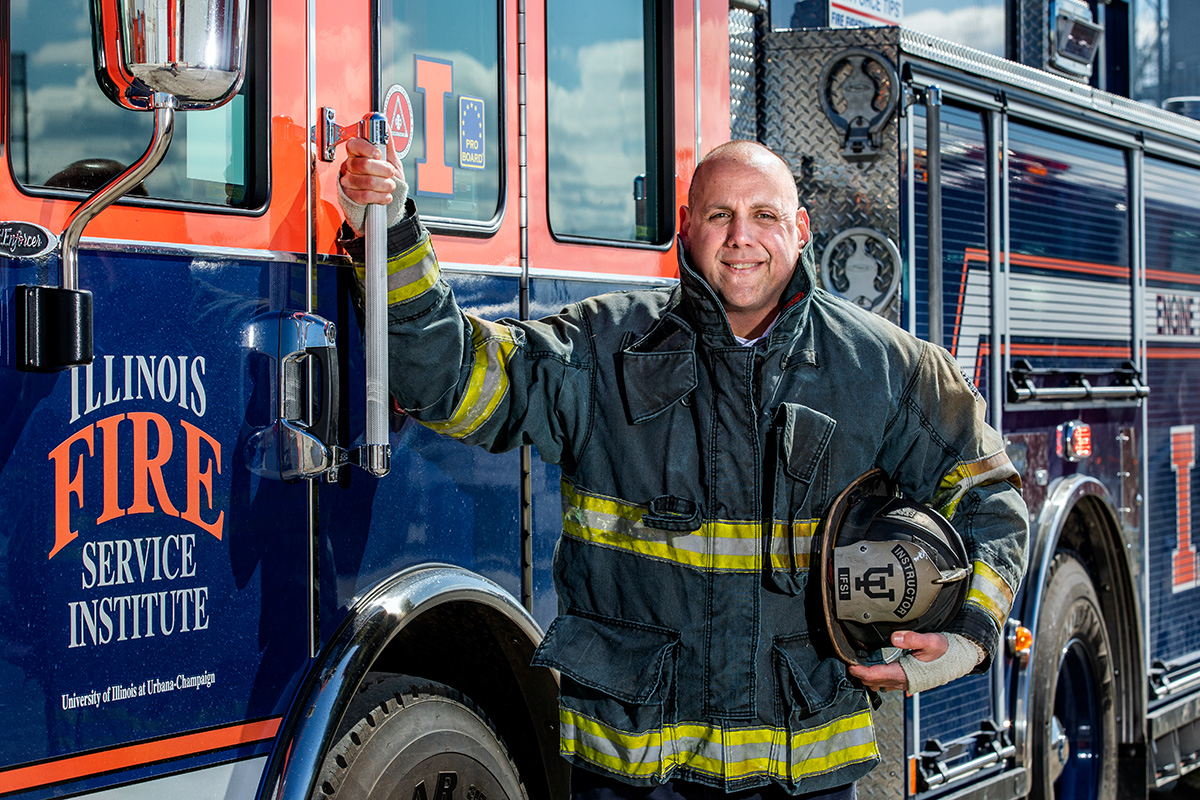 Brian Brauer, dressed in fire resistant equipment, poses for a photo in front of an Illinois Fire Service Institute fire truck.