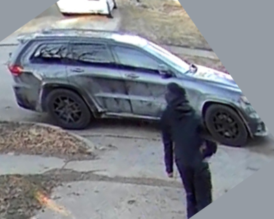 Image depicts a person wearing all black walking toward a dark gray Jeep vehicle with black rims.