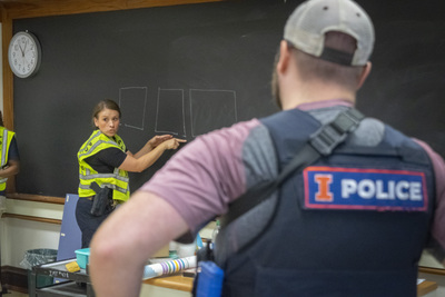 Police officer at chalkboard instructing other police officers.