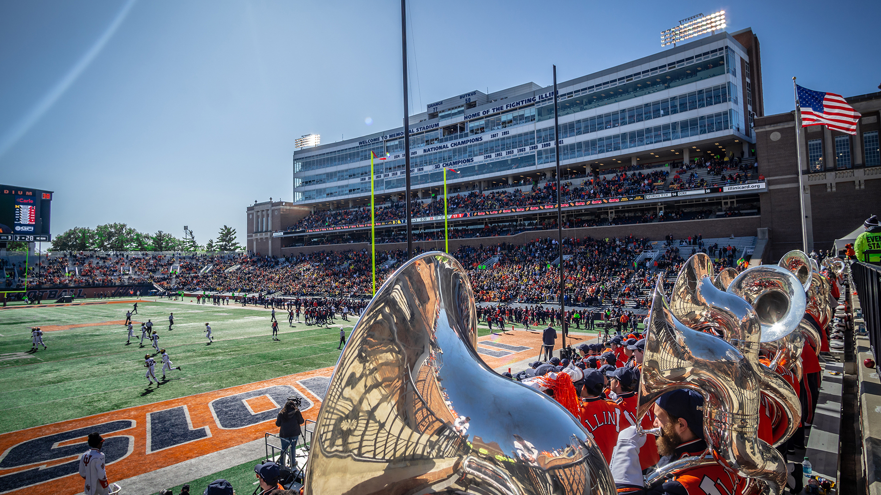 gameday scene at Memorial Stadium includes players on the field and Marching Illini Sousaphones in the stands