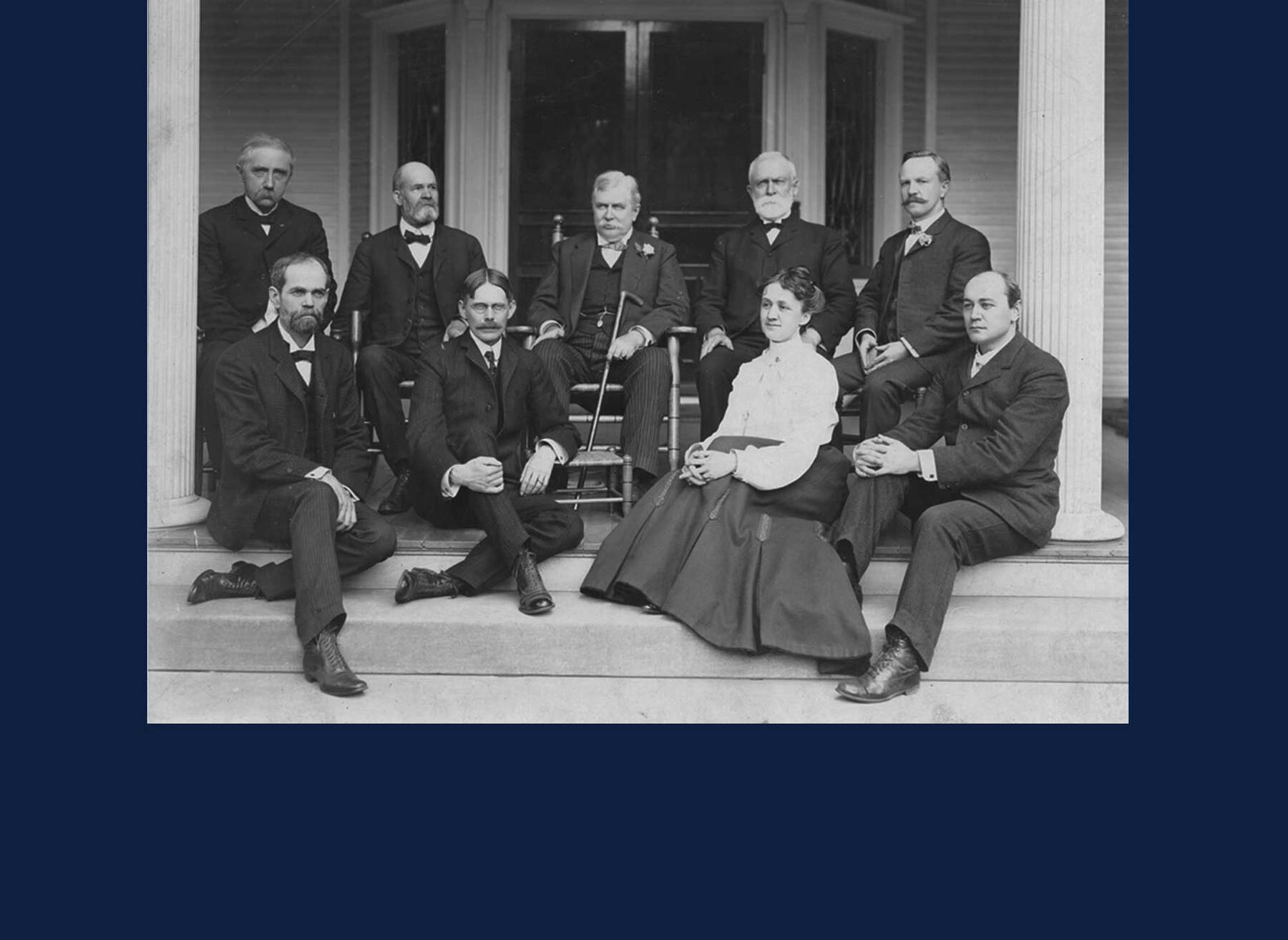 A group of U of I administrators pose for a picture on a porch. The group includes just one woman, first dean of women Violet Jayne. Image via U of I Archives