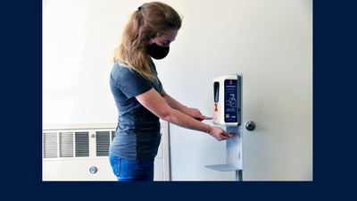 Illinois student uses hand sanitizer station labeled with U of I logo