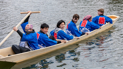 six people in matching blue happi coats launch their traditional Japanese riverboat. Photo by Fred Zwicky