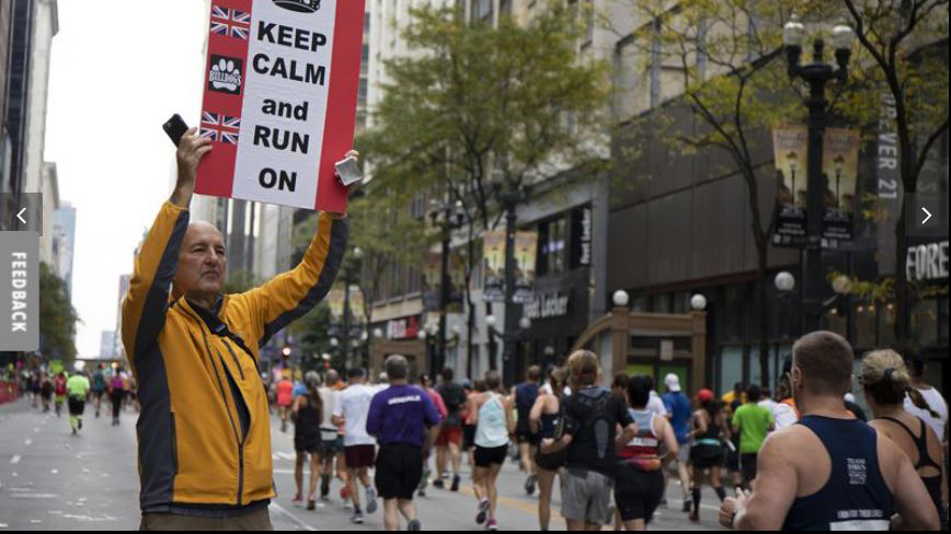 man hold sign reading "Keep Calm and Run On" as marathoners pass