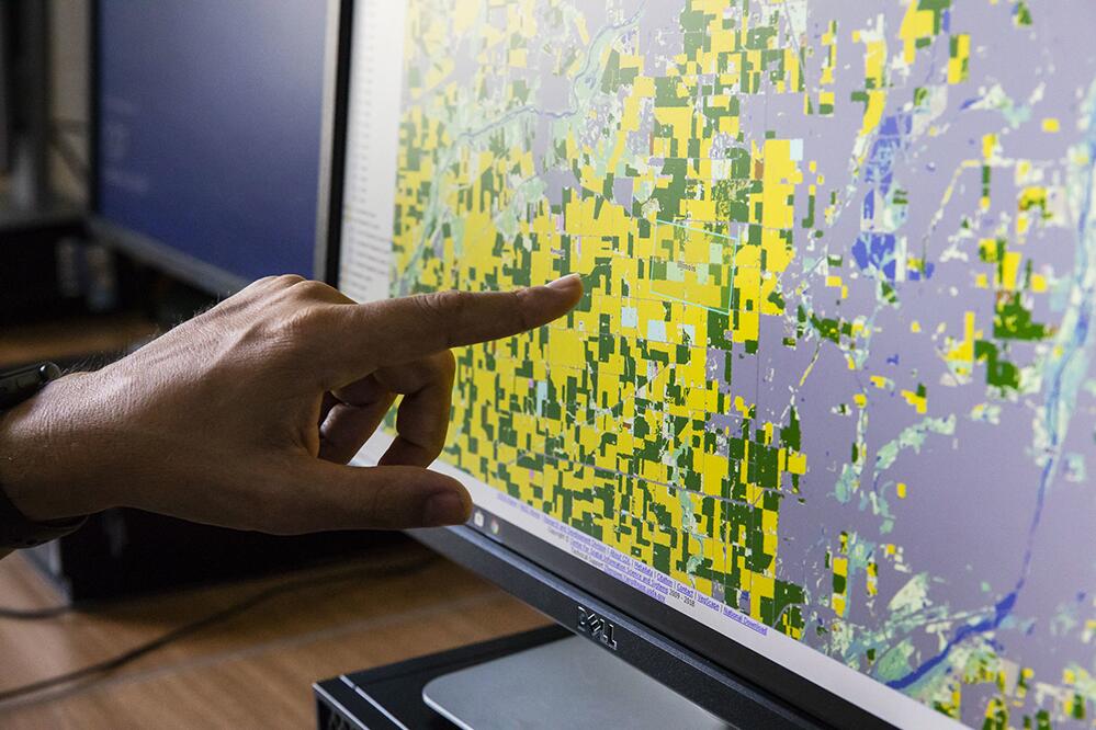 stock image of hand pointing to agricultural land on a computer screen