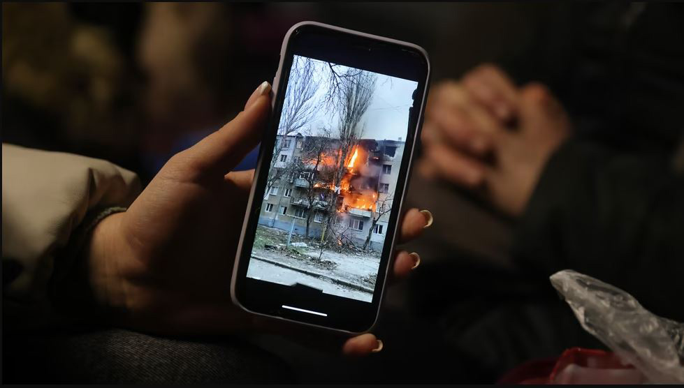 hand holds cell phone displaying images of the war in Ukraine. Photo by Sean Gallup / Getty