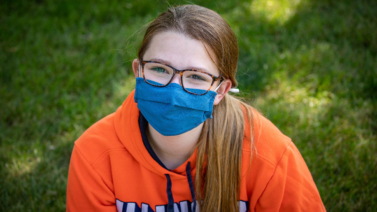 Ilinois student sitting outside wearing a mask.