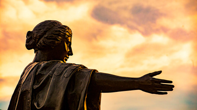 Alma Mater Statue in light of a cloudy orange sunset. Photo by Fred Zwicky