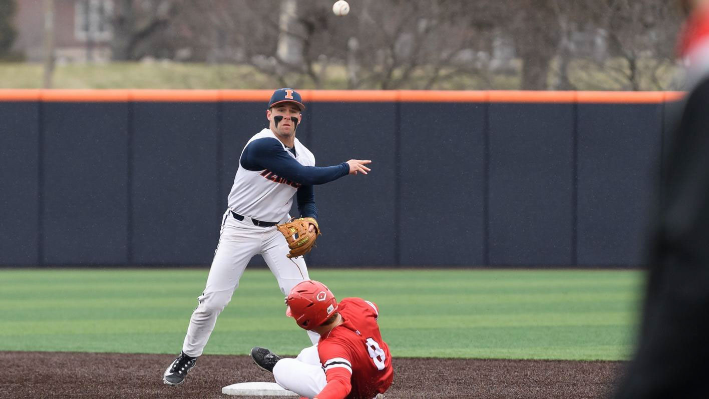 an Illini second baseman, sporting huge patches of eye black, throws to first in an attempt to turn a double play
