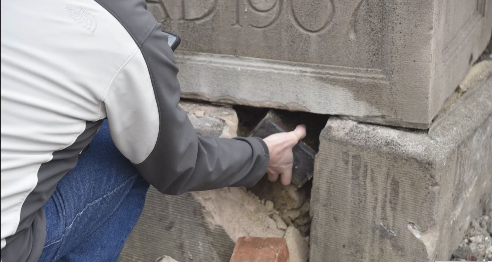 A worker removes a small metal box from the cornerstone, dated 1907, of Illini Hall