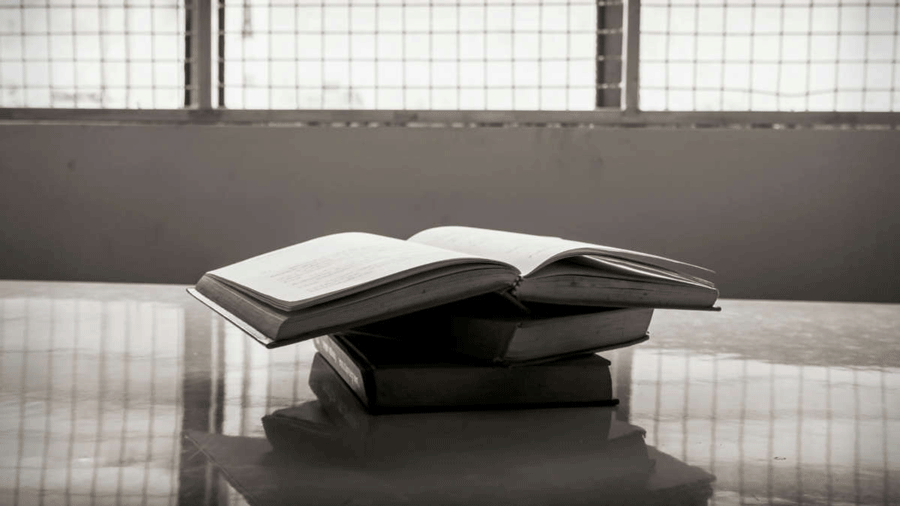 textbook sits on a table before barred windows as in a prison. Photo by TAPUI / ISTOCK / GETTY IMAGES PLUS