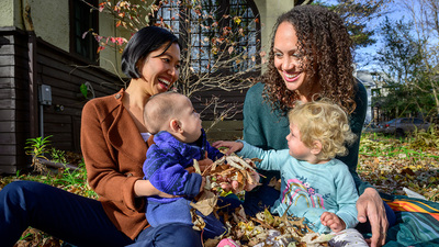 Hoang holds son Nikola, age 7 months; and Tabb Dina holds daughter Cleopatra, age 17 months, while the children play with autumn leaves.  Photo by Fred Zwicky
