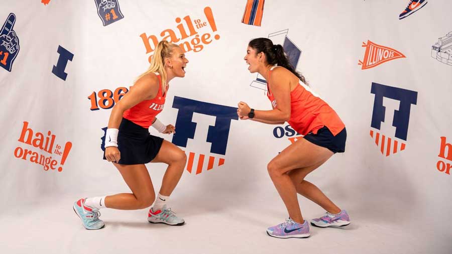 Kate Duong and Megan Heuser pose in front of white screen featuring Illini logos and sayings