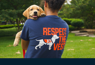 Illini Service Dogs volunteer wearing "respect the vest" t-shirt carries a puppy
