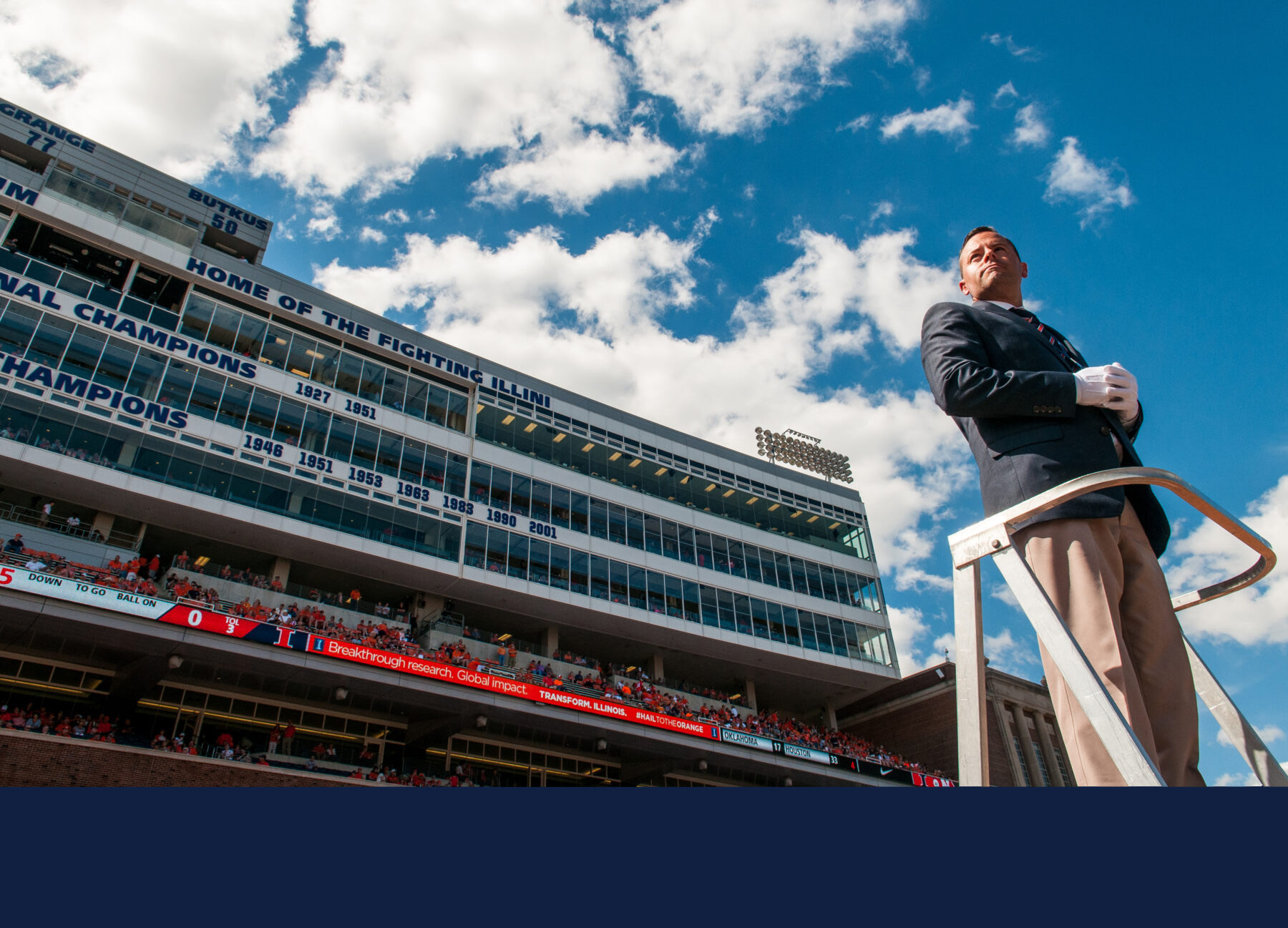 Marching Illini Director Barry Houser stands atop the tower-podium from which her directs the band at Memorial Stadium