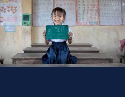 A Cambodian girl proudly displays her work on a chalk tablet.