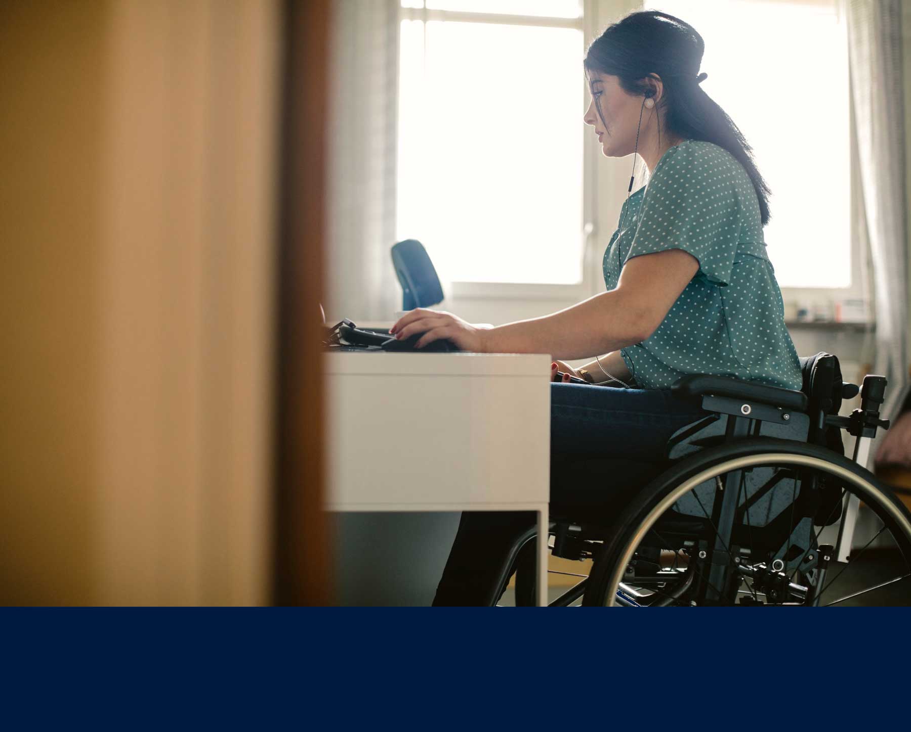 stock image of woman in wheelchair working at a computer with earphones