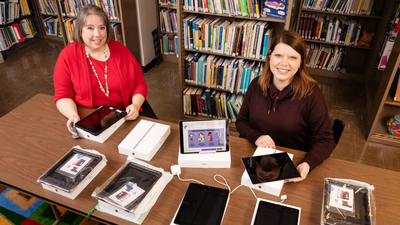 Sarah Isaacs, the librarian of the Early Intervention Clearinghouse, and research information specialist Jill Tompkins show some of the tablet computers and Wi-Fi hotspots that families of infants and children with disabilities or delays can borrow for telehealth visits with providers of early intervention services.