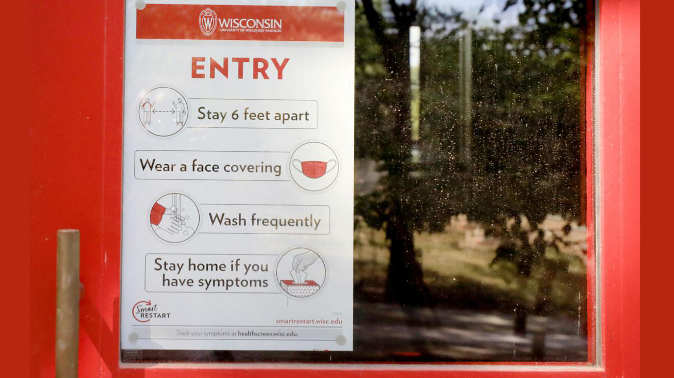 Sign on door at UW-Madison reminds students to wear a mask and socially distance