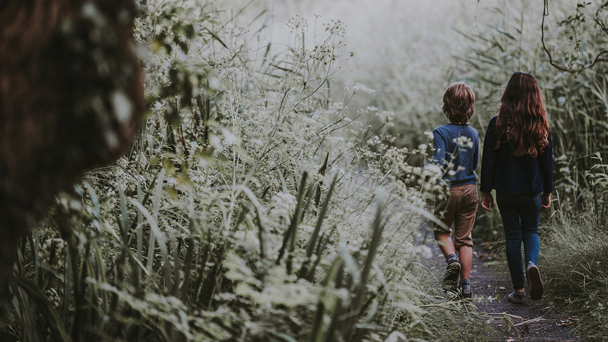 two children walk along a path through a natural area