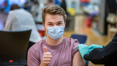A student who works at a COVID-19 testing center gives a thumbs up after receiving a COVID-19 vaccine. Photo by Fred Zwicky