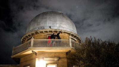 people stand on the catwalk of the observatory and point skyward. Photo by Carly Conway