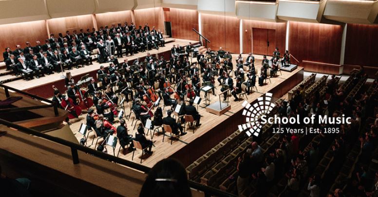 broad view of stage at Krannert Center for the Performing Arts during a symphony concert, with School of Music's 125th Anniversary logo.