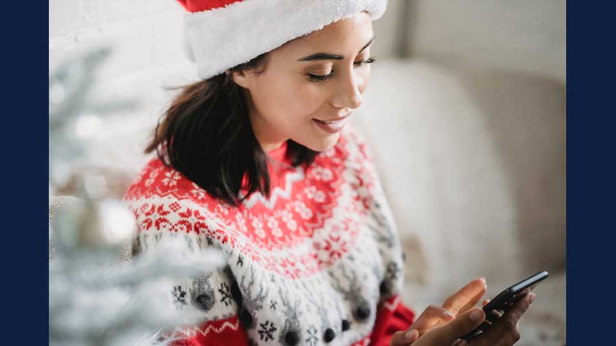 stock image of women in holiday sweater and 'santa' hat looking at cellphone by Julia Larson/Pexels