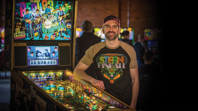 Zach Sharpe stands beside a 'Beatlemania'-themed pinball machine