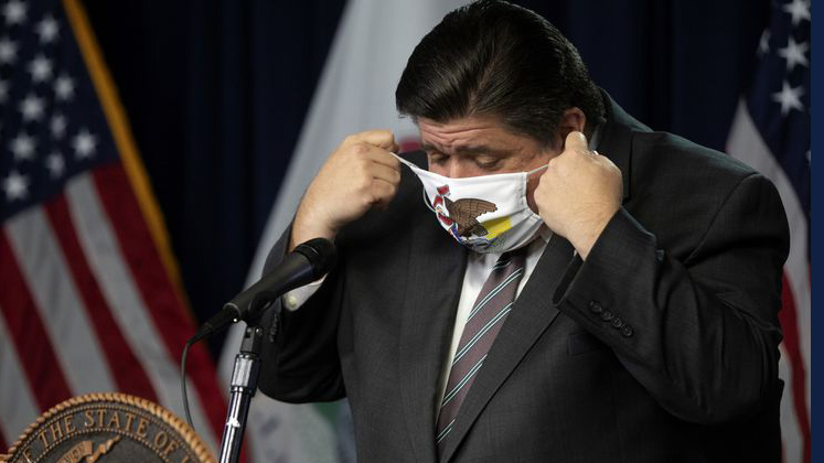 file photo of Governor J. B. Pritzker putting on a face covering