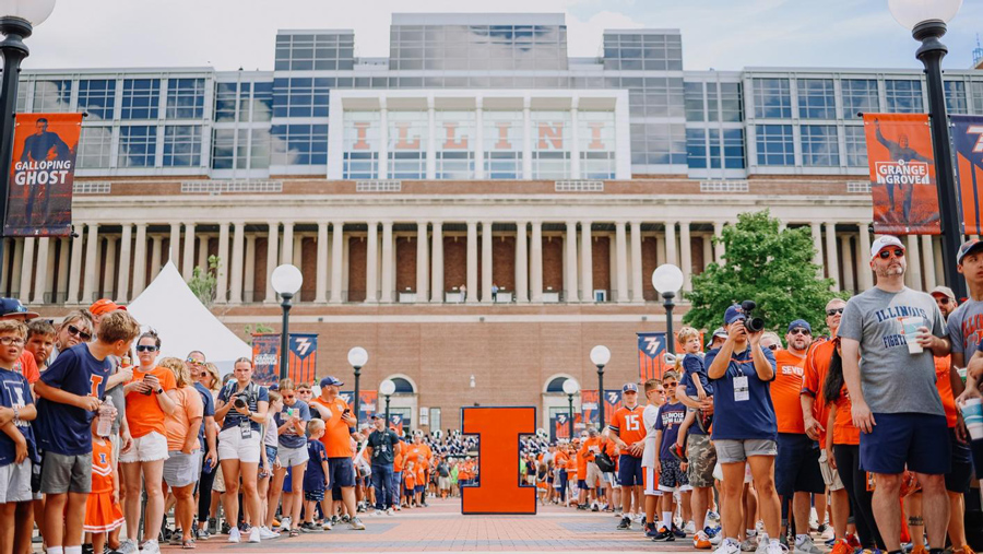 fans line up awaiting the entrance of Illini football players through the Grange Grove tailgating area outside Memorial Stadium