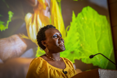 Ngumbi speaks at a podium with an image of a flowering plant projected behind her.