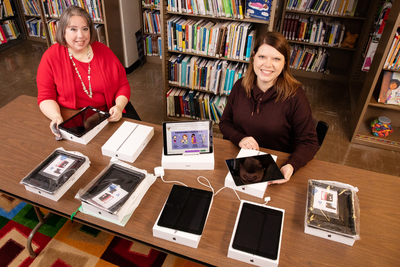 Librarian Sarah Isaacs and research information specialist Jill Tompkins sitting at a table with tablet computers and Wi-Fi hotspots on it.