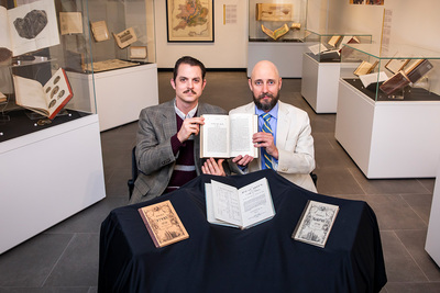 Photo of Neal Davis and Ryan Shosted sitting at a table and holding an open Book of Mormon written in the Deseret Alphabet.