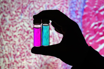 A hand holds two vials of solution, one pink and one blue.