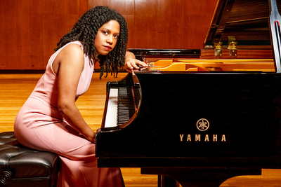 Photo of Rochelle Sennet in a pink evening dress leaning over the keyboard of a Yamaha grand piano.