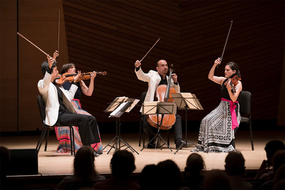 Image of Jupiter String Quartet performing on stage with their bows in the air.