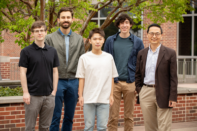 Photo of research team standing together outside in front of a brick wall and building.