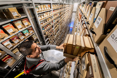 Image of facility coordinator Jimmy Gonzalez using a lift to shelve books at the top of the stacks.