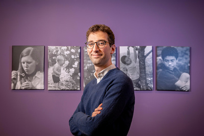 Photo of social work professor Will Schneider standing with arms crossed in front of the logo at the School of Social Work