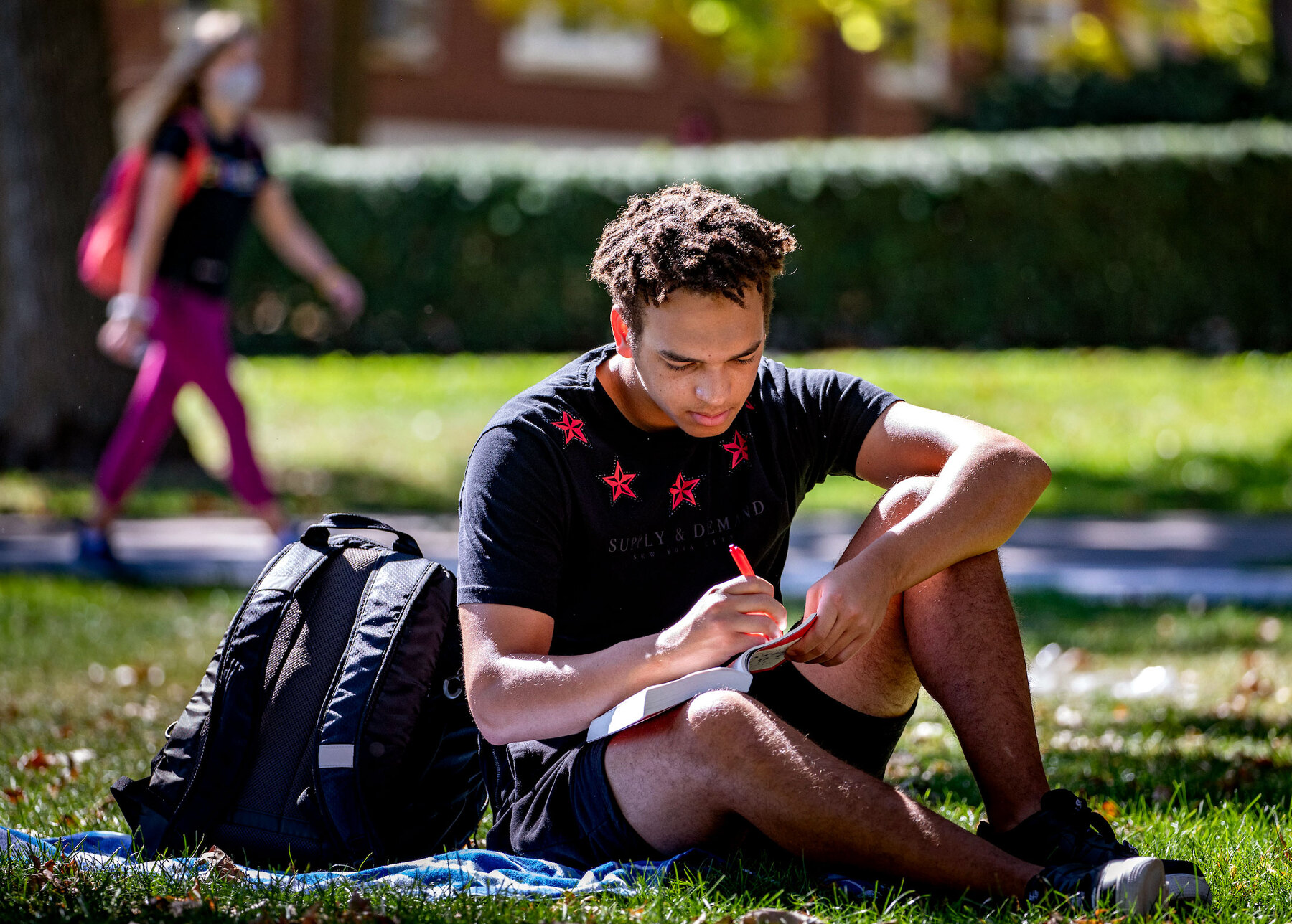 Student in dark shirt with stars sits on the quad and studies.