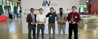 five men pose with awards in front of IIN banner