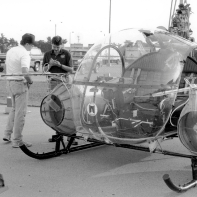 two men stand near a helicopter equipped with cylindrical insect traps