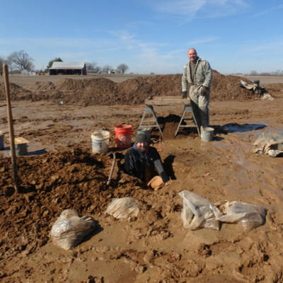 Patrick Durst's head and chest are visible as he stands in an excavation, with Steven Boles standing six feet behind him