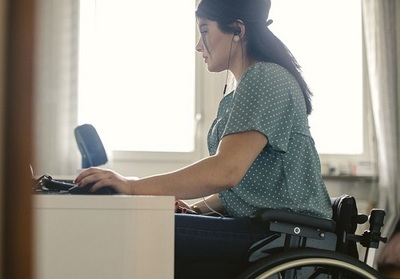 Woman in wheelchair and wearing headset working on computer at a desk