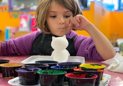 Young girl ponders paint colors in containers in front of her