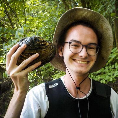 scientist smiling and holding up a freshwater mussel