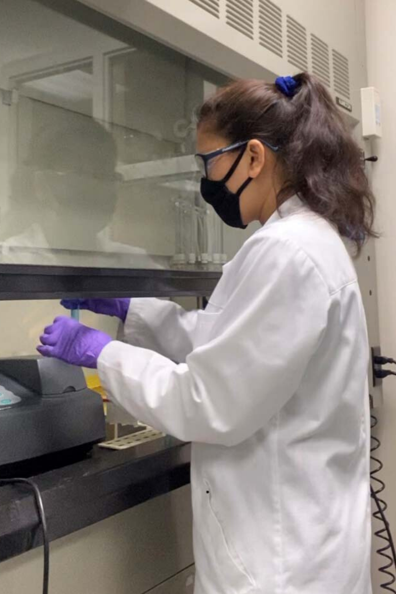 Sarmila Katuwal wears a cloth face covering and standard lab PPE while checking the phosphorous concentration of a designer biochar.