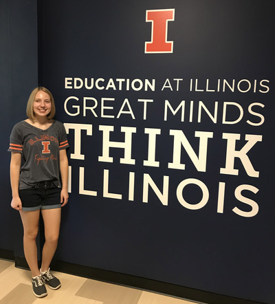 Sara poses next to a mural that reads "Great Minds Think Illinois"