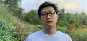 Headshot of Sam Cheng wearing a light crewneck shirt standing in a flowering field